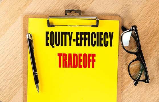 Equity and efficiency tradeoff concept in economics, text yellow paper attached to a clipboard with pen and glasses on a wooden desk