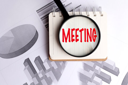 Meeting text viewed through a magnifier on a spiral notebook over business charts, planning, discussion and analysis concept