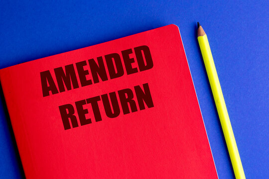 Amended return text on a red notebook beside a yellow pencil on a blue background, tax correction and financial reporting concept
