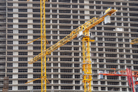 Construction of high buildings and modern skyscrapers in urban city, rapid real estate development, yellow tower cranes at skyscraper construction site, massive high-rise building with apartments.