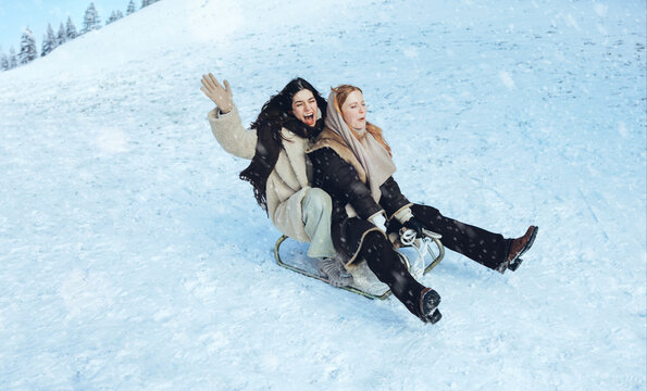 Laughing women sledding with friends on a snowy hill
