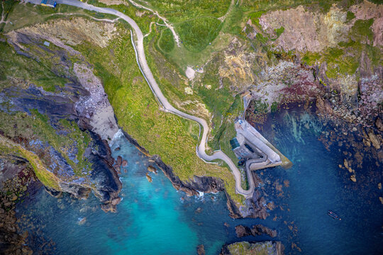 Top down drone aerial view of winding path at Dunquin Pier on rugged cliffs of Dingle Peninsula, County Kerry, Ireland, with turquoise Atlantic Ocean water.