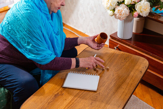 Senior female rolling dice at a table. Calm atmosphere and attention. Concept of relaxation and comfort. Mid shot