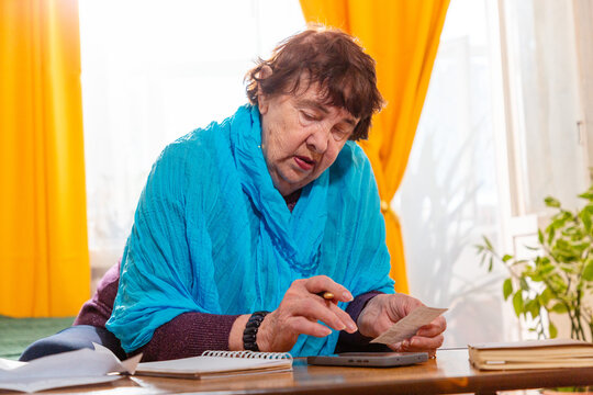 Older Caucasian woman checking monthly expenses with calculator at home. Careful planning and scarcity. Concept of poverty and savings. Mid shot