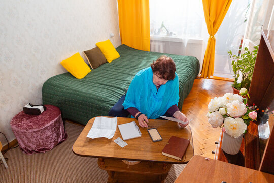 Older Caucasian woman checking household bills at table. Modest lifestyle and concern. Concept of poor pensioner life. Top view