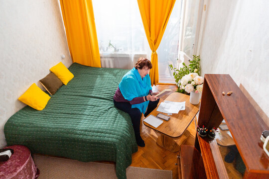 Elderly woman writing budget notes and learning investment strategy at table. Calm discipline and growth. Concept of smart retirement. Wide shot