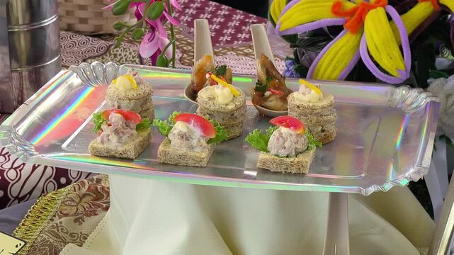 A professional chef plates and garnishes a modern Malay fusion dish during a cooking competition. The beautifully decorated meal is presented on a table for judges to evaluate.
