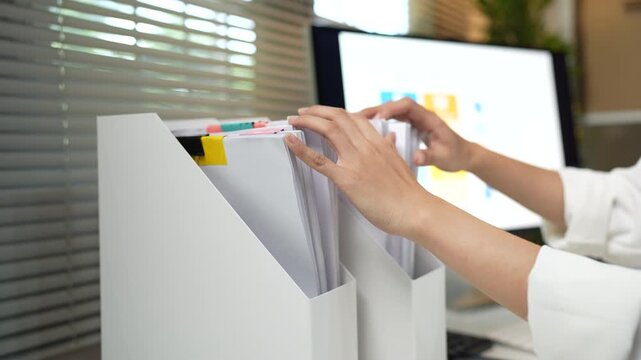 Business professional organizing stacks of documents and reviewing office paperwork for efficient administration and record management.