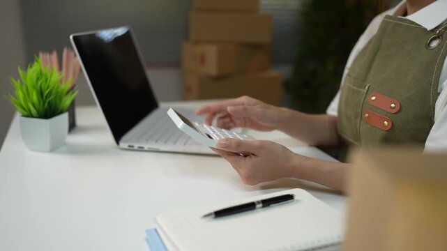 Business professional using a mobile payment terminal while reviewing financial reports and managing sales transactions in an office.