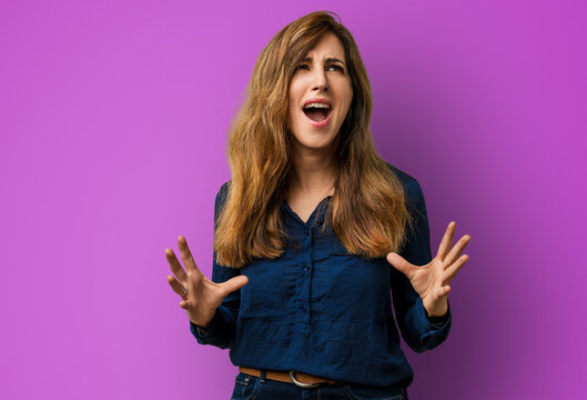 Young woman hispanic in clothes with a mad expression, shouting and yelling with arms raised in a crazy shout - frustration in studio