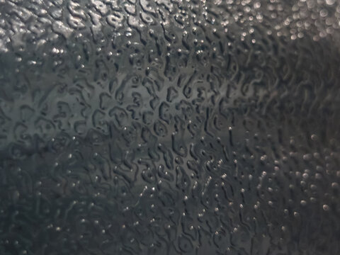 Close-up of a dark charcoal-gray textured surface with irregular raised-looking details and scattered reflective highlights. The abstract pattern and moody lighting