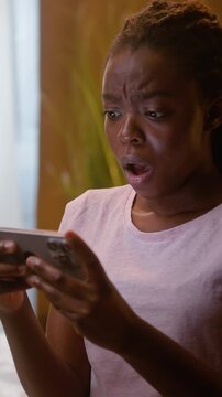 Shocked African American woman watching video on smartphone at home bedroom night upset disappointed ethnic female girl using cellphone negative reaction mobile phone gaming failure losing game indoor