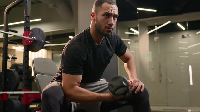 Strong African American male bodybuilder lifting dumbbell in gym during strength workout powerful man athlete rowing heavy weight training arms and muscles sport club healthy fitness lifestyle indoor