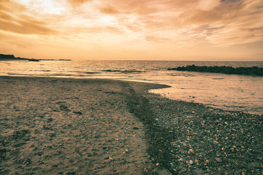 Sunset at the sandy beach with breakwater by the sea.