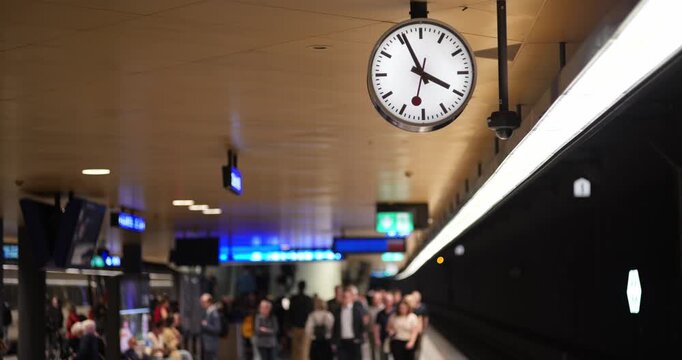 Zurich, Switzerland, October 6, 2026. A sharp station clock hangs above blurry commuters walking towards the camera on an underground platform.