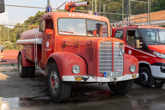 June 26, 2026, Petrovac, Montenegro, Vintage red fire truck with water tank parked beside modern emergency vehicles at a sports facility in daylight