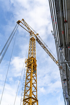 Yellow tower crane jib photographed from below against bright blue sky with clouds