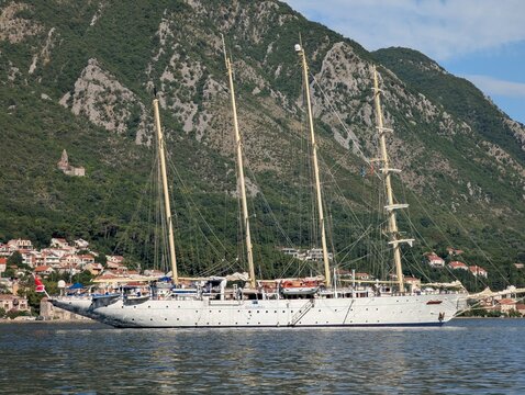 July 4, 2026, Kotor, Montenegro, Large sailing ship anchored in calm waters near a coastal town with mountains and greenery in the background