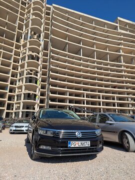 June 28, 2026, Petrovac, Montenegro, Black Volkswagen car parked in front of an unfinished concrete building with graffiti and clear blue sky