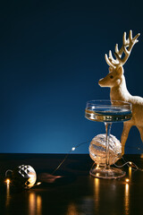 Champagne coupe glass with holiday decorations and golden reindeer against blue background © ShapeImages