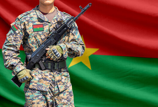 Burkina Faso flag with soldier in military uniform holding assault rifle in front of it