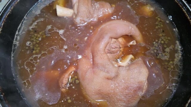 Pork knuckle simmering in savory broth with peppercorns top view