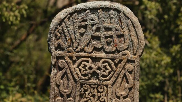 Ancient medieval Muslim gravestone with intricate hand-carved Arabic calligraphy script, geometric patterns, and traditional floral ornaments. kayrakt close-up shot of weathered stone stele relief..