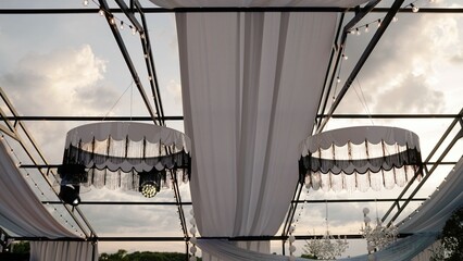 Stylish black and white chandeliers with fringe hanging from outdoor event tent frame with string lights and drapery, event decoration © Ruslan