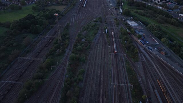 Aerial drone view from above of a train traveling through an extensive railway network in England, with multiple parallel tracks, junctions and overhead electrical infrastructure visible at dusk.