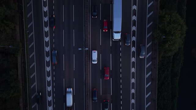 Top-down drone view of cars, vans and a large truck moving along a multi-lane motorway in England. Traffic flows through marked lanes, creating a geometric transportation pattern and showing modern ro