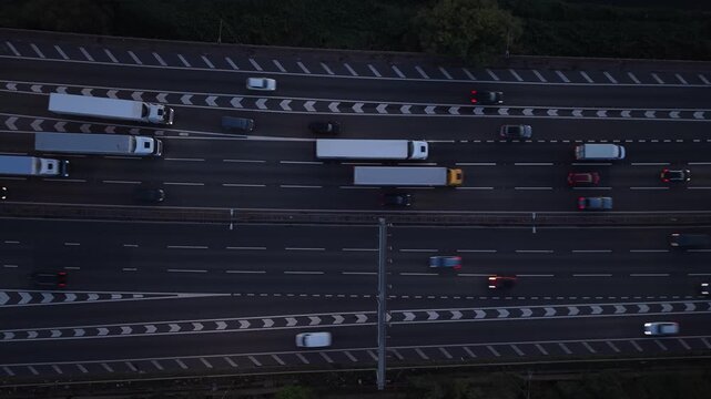 Top-down aerial drone view of trucks, vans and cars travelling along a busy multi-lane motorway in England at dusk. Commercial freight vehicles and everyday traffic create a strong geometric pattern,