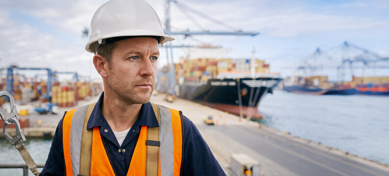 Port worker in hard hat and safety harness at container terminal, maritime PPE and fall protection