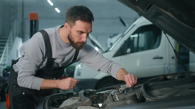 Professional Caucasian man mechanic examining motor under open car hood in workshop male vehicle technician checking engine condition auto repair specialist doing maintenance mechanical check service