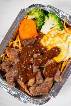 Beef noodles with fried egg and fresh vegetables packed in aluminum foil takeout tray