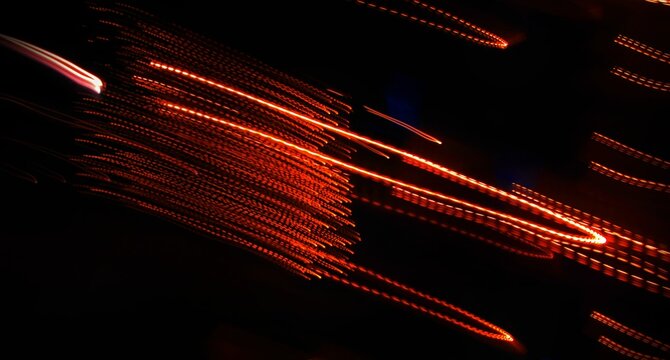 Abstract light trails on a black background with a motion blur effect. Neutral graphic background.