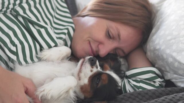 Young girl affectionately cuddling and kissing a Cavalier King Charles Spaniel puppy while relaxing in bed at home, showing love, tenderness and a close bond between child and pet