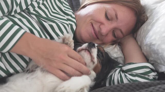 Young girl affectionately cuddling and kissing a Cavalier King Charles Spaniel puppy while relaxing in bed at home, showing love, tenderness and a close bond between child and pet