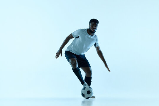 Alert male athlete dribbling soccer ball in blue studio. Youth coaching resources, personal training concept.