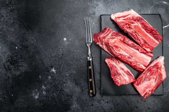Raw beef short ribs chunks with rich meat and bone texture on slate. Minimal dark background for stew broth and slow cooking.