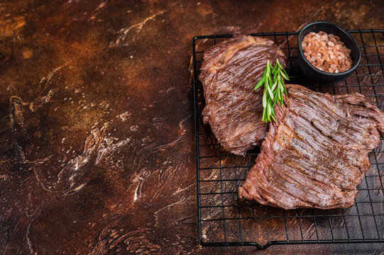 Juicy grilled beef steak bavette flap cut resting on rack with rosemary and salt crystals gourmet barbecue meat concept on textured brown backdrop