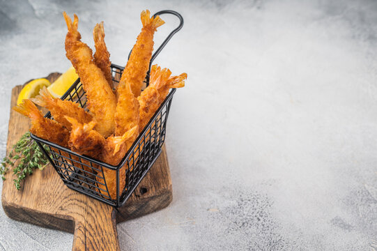 Panko fried prawns or ebi fry in metal basket, crunchy deep fried seafood snack styled with herbs and citrus on light background, top view composition.