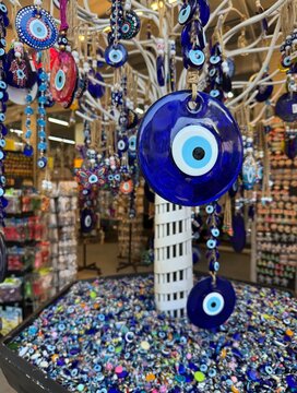 A traditional Turkish blue evil eye bead (nazar boncuğu) hanging in a souvenir shop, surrounded by a display tree and a large bowl filled with various glass protective amulets and talismans.