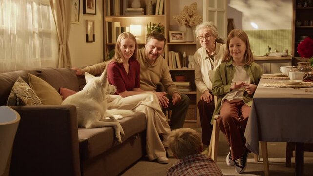 Tilt up view of Caucasian child playing charades before multi-generational Caucasian family and dog at home. Footage suits family lifestyle campaigns, real estate ads, and domestic leisure marketing
