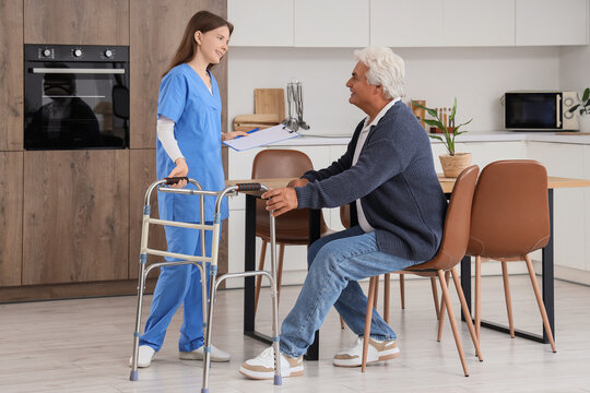 Home care and elderly assistance, nurse helping senior man with walker in kitchen for medical support and rehabilitation during recovery at home