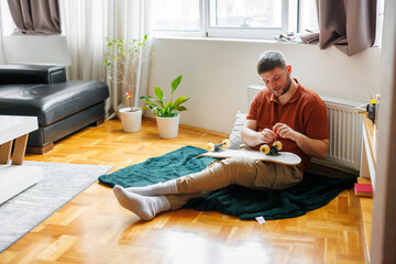 Man fixing the wheels on skateboard while relaxing at home © Impact Photography