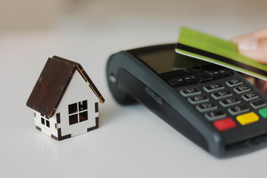 Miniature house beside a payment terminal and credit card, representing real estate purchase, mortgage financing, and homeownership.