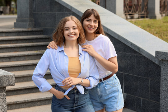 Friendship and female bonding, two happy young women standing together outdoors on city stairs with casual summer clothing and genuine smiles