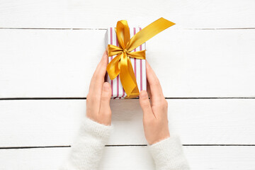Fototapeta premium Gift giving and celebration, person holding a striped present with a gold ribbon on a white wooden table for holidays and special occasions