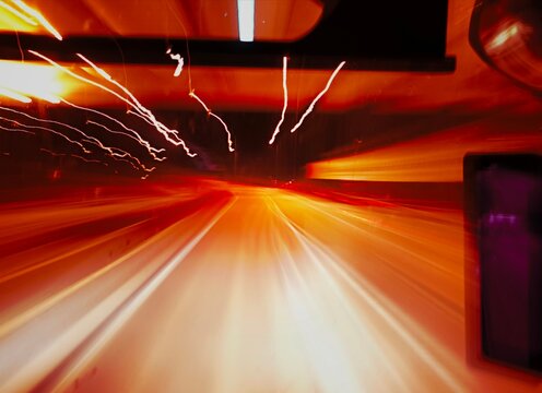 Blurred vehicles creating glowing red and white light trails on a dark wet road at night, captured with long exposure technique.