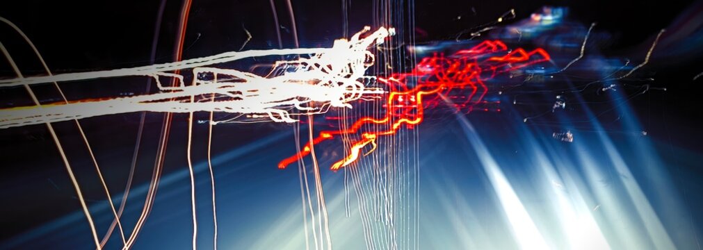 Blurred vehicles creating glowing red and white light trails on a dark wet road at night, captured with long exposure technique.